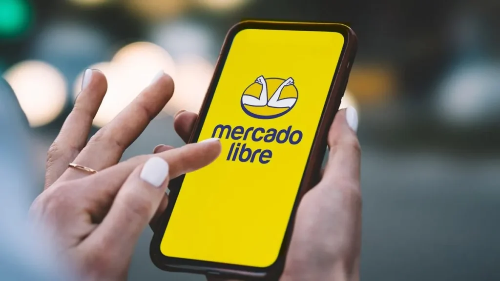 Una persona interactúa con la pantalla de su celular, la cual muestra el logotipo amarillo y azul de Mercado Libre.