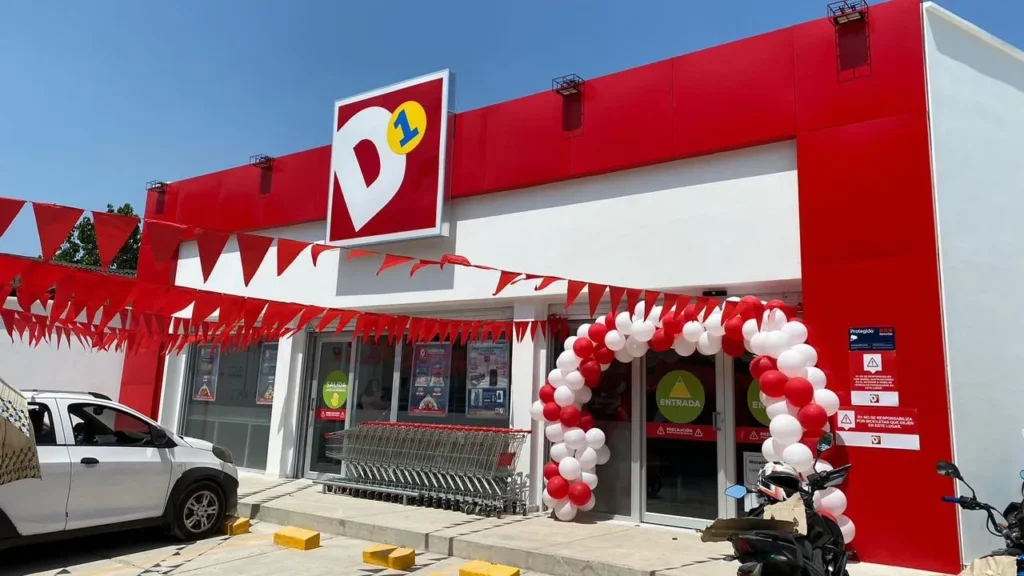 Fachada exterior de un supermercado Tiendas D1 con su letrero oficial rojo y una decoración de globos en la entrada.